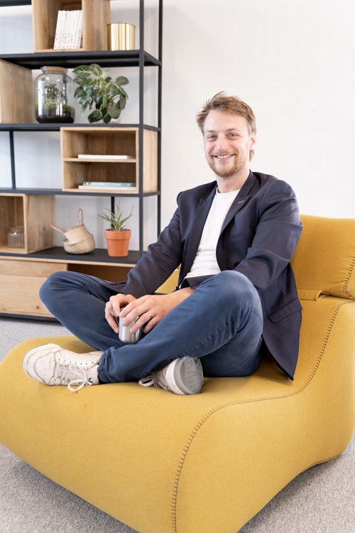 Portrait de Mathieu Doumalin, assis sur un fauteuil jaune et souriant.